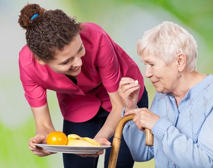 Betreuerin reicht Klientin ein Teller mit Obst